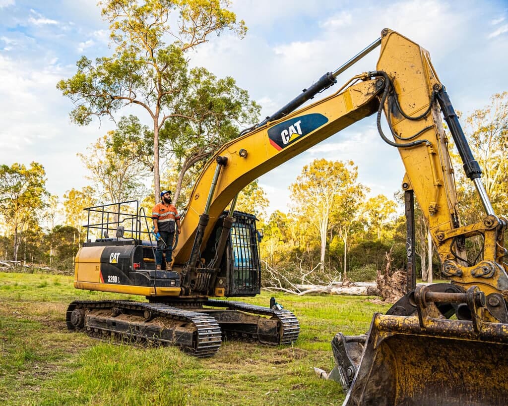 Operator standing on a CAT 329D excavator on a bush block