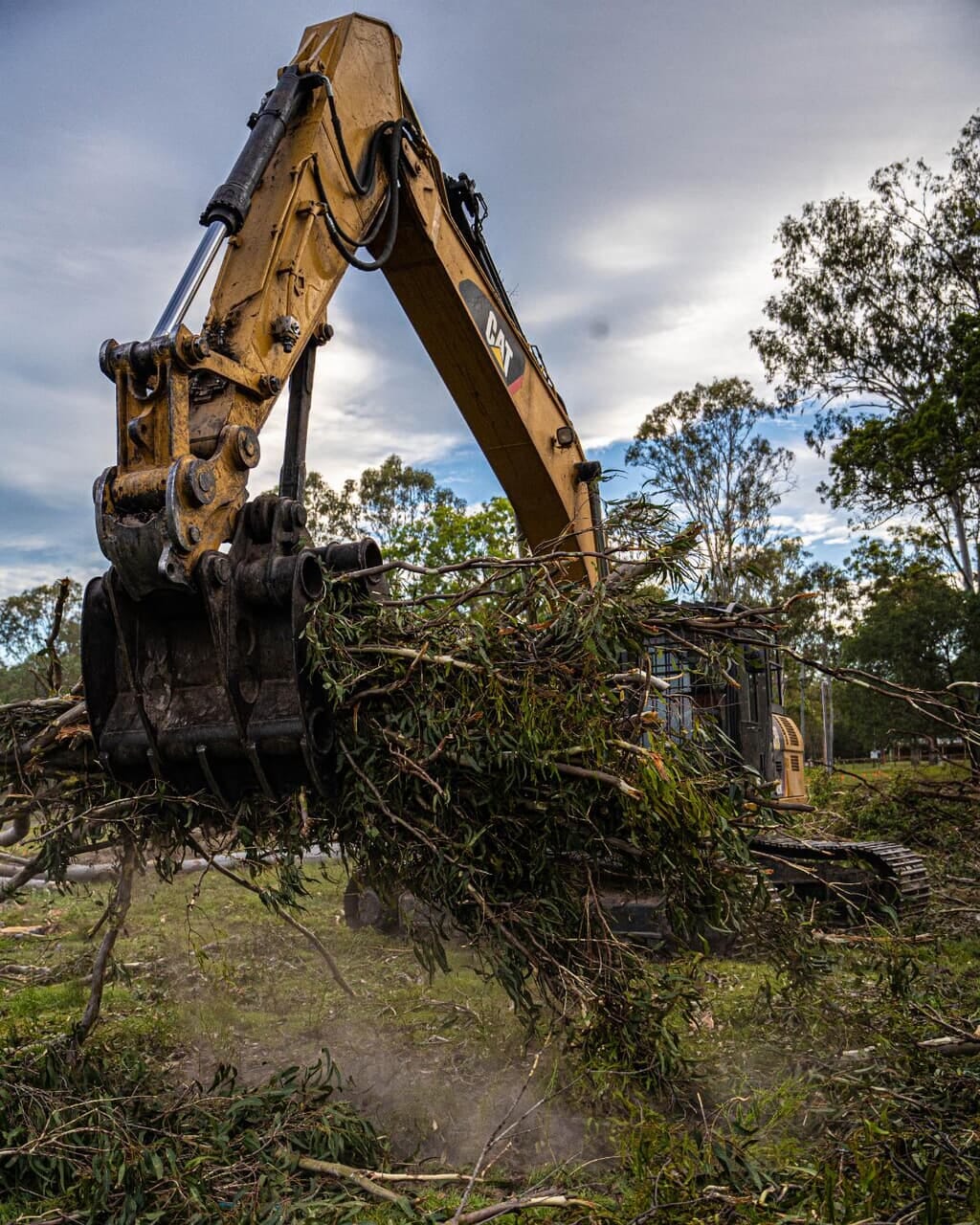 Excavator grapple lifting cleared vegetation