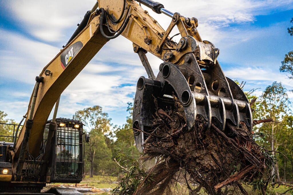 Excavator grapple lifting a root ball